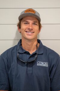 Trevor E, Project Manager and Lead Carpenter at Citadel Enterprises, smiling in a blue polo shirt with company logo and sunglasses.